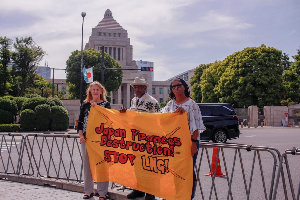 Texas community leaders in front of the Tokyo Diet. They hold up a bright yellow sign that reads, "Japan finances destruction. Stop LNG!)