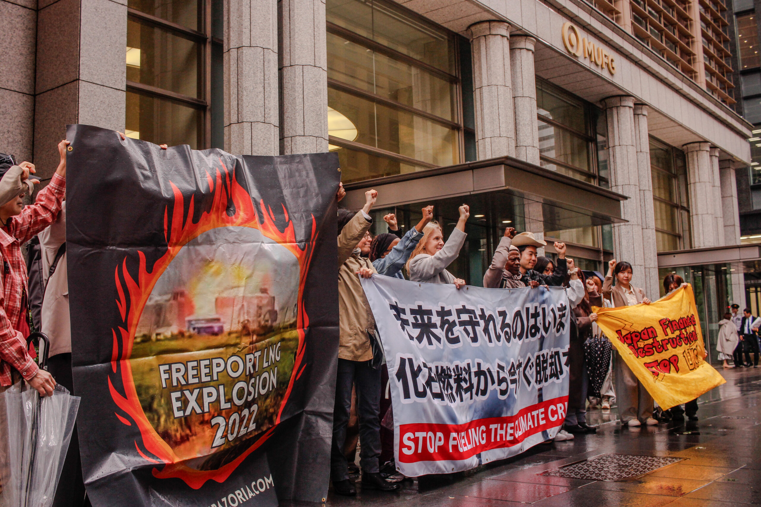 Activists hold signs protesting Japan's funding of fossil fuels.